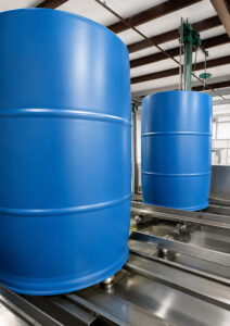 Plastic barrels traveling on the conveyor track inside an LS Industries Poly Washer while high-pressure water jets clean the interior surfaces for thorough contaminant removal.
