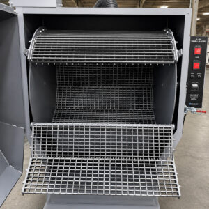 Inside view of a tumbler blaster with the basket open, showcasing the tumbling drum designed to hold and process parts during abrasive blasting operations.