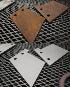 Alt Text: Side-by-side comparison of parts before and after manual abrasive blasting inside an air blast cabinet, showing the removal of rust, paint, and surface contaminants.
