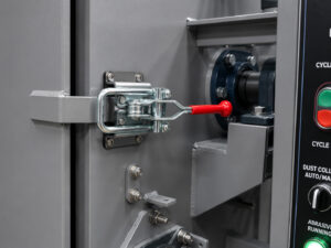 Heavy-duty door latch on a rubber belt blaster designed to securely seal the blast cabinet during abrasive blasting operations.