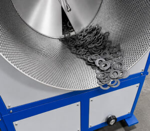 Exit view of a corn cob drying system showing dried parts discharging from the machine after moisture removal and media separation.