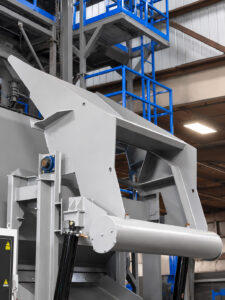 Optional hydraulic dumper loading heavy parts into a slat blaster, simplifying material handling and improving loading efficiency for large industrial components.