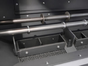 Inside view of a fixed basket blaster showing the basket support rollers and side-mounted blast wheels used to rotate parts and deliver abrasive blasting coverage.