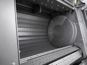 Inside view of a slat blaster showing the steel slat conveyor, blast zone, and abrasive blasting chamber where large and heavy parts are surface prepared.