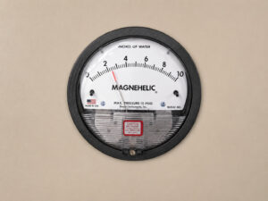 Magnehelic differential pressure gauge mounted on a downdraft table, used to monitor filter condition and airflow performance within the dust collection system.