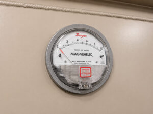 Magnehelic differential pressure gauge mounted on a powder coat booth, providing real-time monitoring of airflow and filter performance within the booth's filtration system.