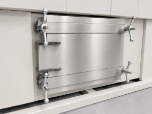 Heavy-duty submarine-style door at the tank entrance of a monorail flow-through washer, providing secure sealing and containment of cleaning solution within the wash chamber.