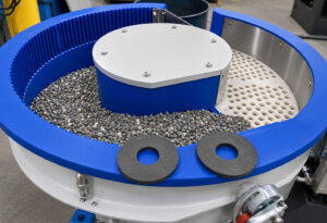 Top-down view of a vibratory bowl finishing system showing the processing chamber, spiral track, media, and part flow path used during finishing operations.