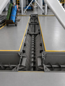 T-shaped auger system in a blast room used to collect and transport spent abrasive media from multiple directions to the media recovery system.