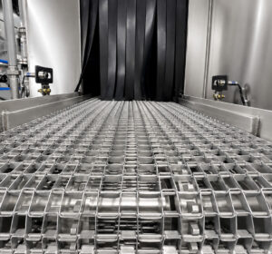 Chain mesh belt conveyor inside a flow-through washer transporting parts through wash, rinse, and drying stages while allowing complete cleaning coverage from all directions.