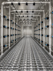 Interior view of a chain mesh belt flow-through washer featuring high-pressure spray nozzles positioned above, below, and along the sides of the conveyor for complete part cleaning coverage.