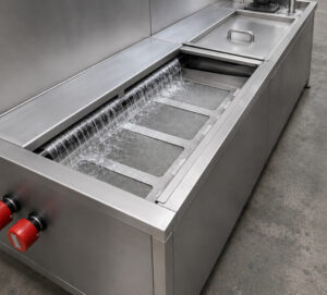 Angled view of an oil skimmer on a monorail flow-through washer continuously removing floating oils and contaminants from the wash solution to maintain cleaning performance.