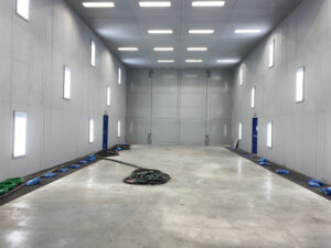 Empty interior of an industrial blast room showing the blasting area, media recovery floor, lighting, and workspace without any parts or equipment being processed.