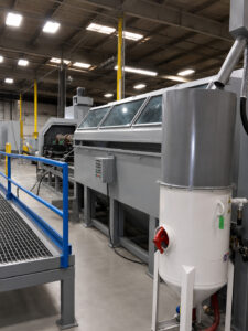 Angled view of a crankshaft blaster designed to automatically clean and prepare crankshaft surfaces using abrasive blasting technology.