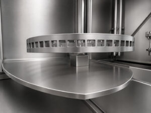Drain tray located beneath the door-mounted rotating table of a batch table washer, designed to capture and return cleaning solution to the wash system during loading and unloading.
