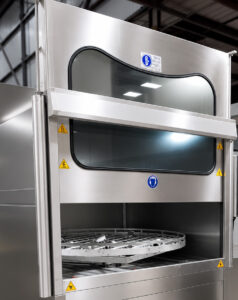 Automatic push-up door on a stainless steel washer providing powered vertical opening and closing for safe, efficient loading and unloading of parts.