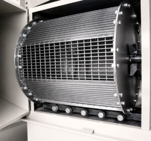 Rotating basket inside a tumble washer holding parts during the cleaning cycle while continuously tumbling components for complete cleaning coverage.