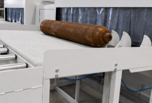 Cylinder positioned at the entrance of a flow-through cylinder blaster and held in place by an entrance stopper before entering the blasting chamber.