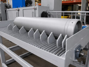 Exit section of a flow-through cylinder blaster showing a freshly blasted cylinder stopped by an exit stopper to prevent it from rolling off the machine.