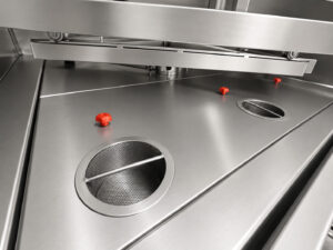 Industrial filtration screens and filter basket located at the bottom of a stainless steel washer, designed to capture contaminants and protect the cleaning system.