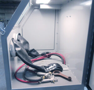 Interior view of a glass bead blaster showing the blasting chamber, nozzle, gloves, and media flow used for precision surface finishing.