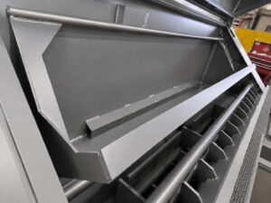 Kick-out bar on a cylinder shot blaster used to push processed cylinders out of the blasting area for unloading or transfer.
