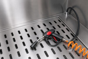 Pressure washer spray gun resting inside the bottom of the wash cabinet, ready for high-pressure cleaning of industrial parts and components.