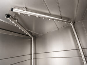 Overhead spray headers and nozzles inside a stainless steel washer delivering high-pressure cleaning solution from above for complete part coverage and effective contaminant removal.