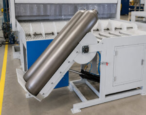Freshly blasted cylinders being removed from a flow-through cylinder blaster using an upender/downender for safe and efficient material handling.