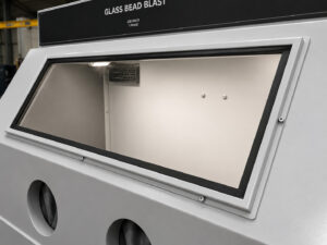 Angled view of the viewing window on a glass bead blasting cabinet, providing operators with a clear line of sight into the blasting chamber.