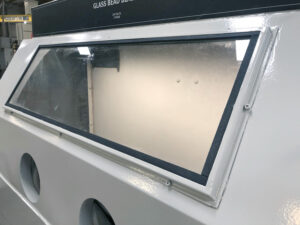 Viewing window on a glass bead blaster allowing operators to clearly see parts during abrasive blasting inside the cabinet.