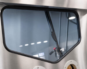 Viewing window with integrated wiper system on an industrial pressure washer, allowing operators to maintain clear visibility inside the wash chamber during cleaning operations.