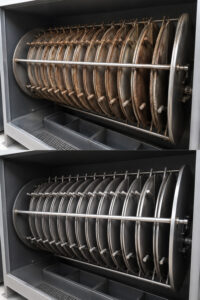 Side-by-side comparison of drum lids before and after processing through a batch drum lid blaster, showing the removal of rust, paint, and surface contaminants.