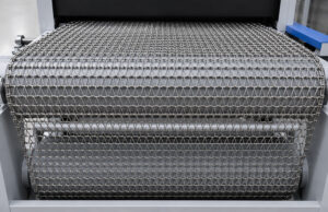 Exit view of a chain conveyor on a flow-through blaster transporting freshly blasted parts out of the blast chamber for the next stage of production.