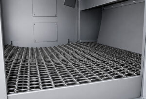 Chain conveyor inside the blast zone transporting parts through high-velocity abrasive media for automated cleaning and surface preparation.