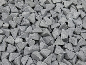 Large pile of polyhedron ceramic vibratory media used for aggressive deburring, edge radiusing, cleaning, and surface finishing of complex metal components.