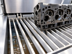 Engine cylinder head positioned inside an LS Industries Stainless Steel PAX Agitation Washer for thorough removal of oil, grease, carbon, and other contaminants.
